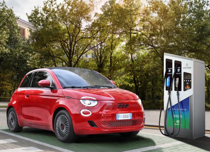 Two happy young beautiful women are talking to each other until their electric car is charging at the charging station situated in the car park.